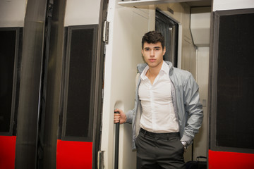 Naklejka na ściany i meble Handsome young man on train, standing in open door threshold