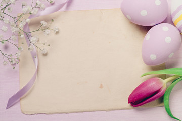 Colorful Easter eggs and flowers on old sheet of paper with spac