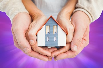 Composite image of couple holding small model house in hands