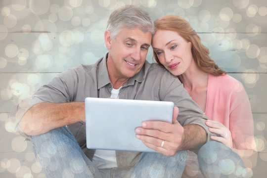 Composite image of casual couple sitting using tablet