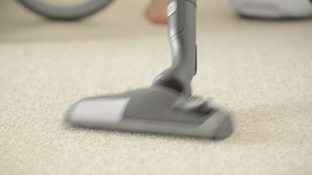 Woman using vacuum cleaner to vacuum carpet in shallow focus