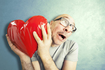 Man in love holds a red heart shape pillow - obrazy, fototapety, plakaty