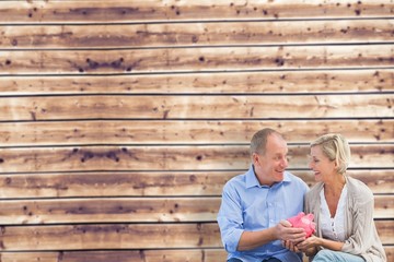 Composite image of happy mature couple holding piggy bank