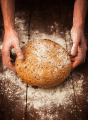 Baker hands with fresh bread on table