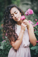 Beautiful young woman in a pink dress posing in a rose garden