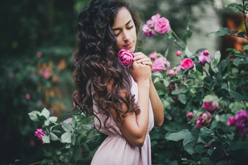 Beautiful young woman in a pink dress posing in a rose garden