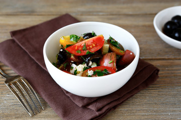 Salad with tomatoes, olives and cheese in a white bowl