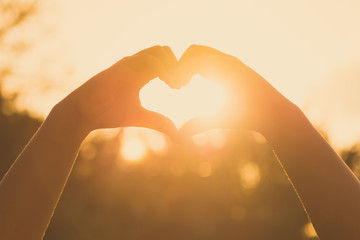 hands forming a heart shape at sunset