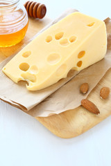 Piece of cheese on a board with almonds and honey