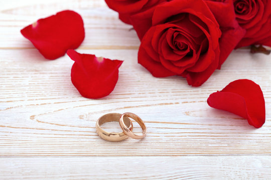 Wedding rings and wedding bouquet of red roses petals.