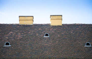 Old tiled roof with chimneys and dormers on blue sky background
