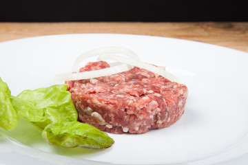 Raw cutlet, onion and salad on a white plate