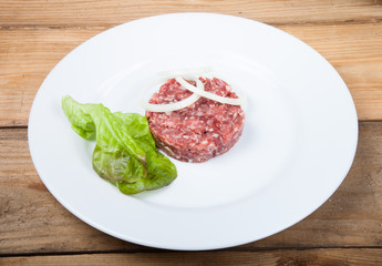 Fototapeta premium Raw cutlet, onion and salad on a white plate