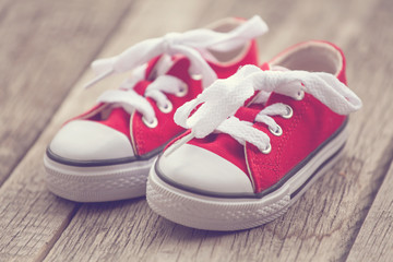 Red baby sneakers on wooden background. Vintage style image