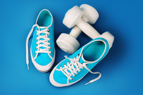 Turquoise gym shoes and white dumbbells on a blue sports mat