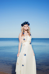 Fototapeta na wymiar Girl near the sea in a white dress and wreath 