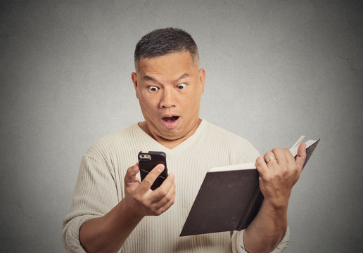 shocked middle aged man looking at phone holding book 