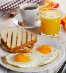 Breakfast with two fried eggs, toasts, juice and coffee.
