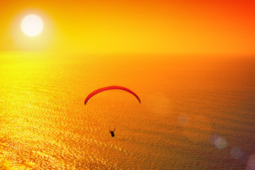 Silhouette of paraglider soaring over sea at sunset