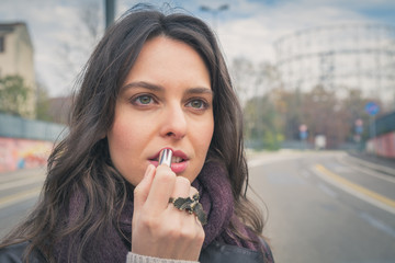 Beautiful young brunette putting on lipstick in the city streets