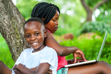African kids under tree with laptop.