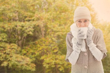 Composite image of woman in warm clothing holding mugs