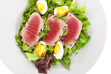 Delicious tuna steak with fresh green salad on white plate.