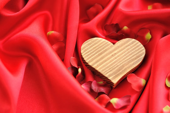 Wooden Heart on a background of red petals and satin