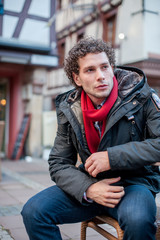 Fototapeta premium Junger Mann sitzend auf einer Bank Urbano Locken City