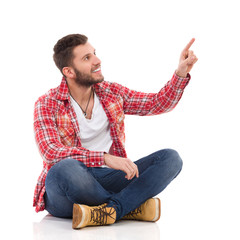 Male student in lumberjack shirt sitting and pointing up