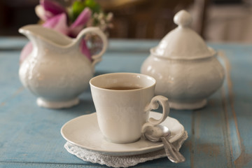Pretty coffee cup, sugar bowl and creamer on old table.