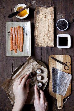 overhead shot of hands slicing sushi and ingredients on table