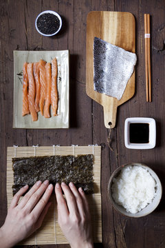 hands rolling sushi and ingredients on table