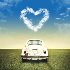 Couple driving on a white car under clouds heart shape