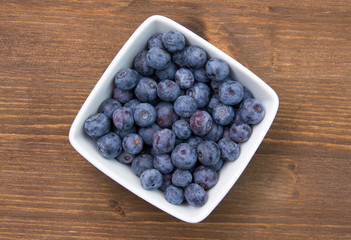 Blueberries on square bowl on wooden table seen from above