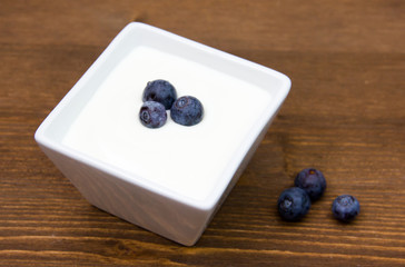 Yogurt with blueberries on square bowl on wooden table