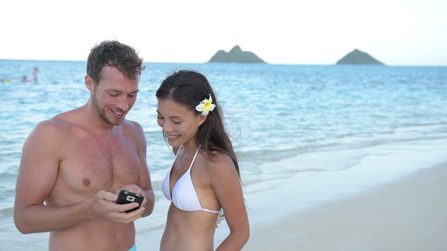 Couple using mobile cell smart phone on beach