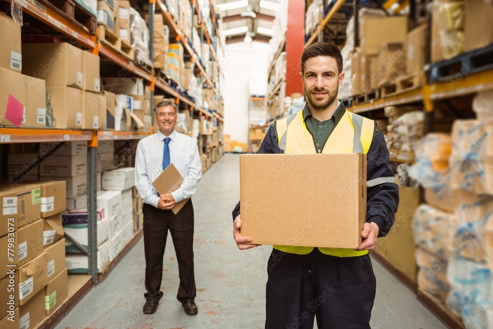 Wall mural warehouse worker smiling at camera carrying a box