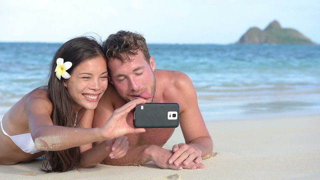 Beach couple taking funny selfie with smartphone