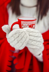the girl in mittens holds a red cup in hand