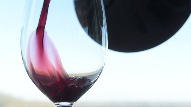 Glass being filled with red wine with carafe on white background