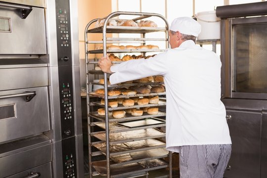 Smiling baker pushing tray of bread