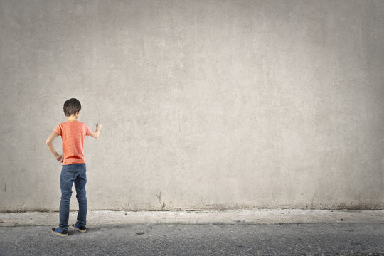 Young boy writing on a blank wall