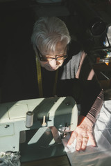 The old woman sews on the sewing machine