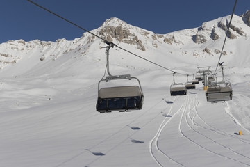 Snowboarders and skiers riding up a ski lift in Dolomites