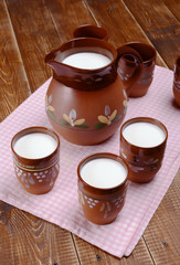 Clay jug and three cups of milk on a wooden table.