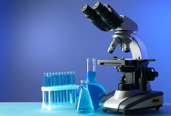 Microscope and test tubes on table, on color background