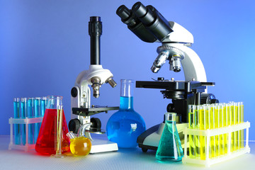 Microscopes and test tubes on table, on color background