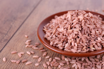 Red rice on plate on wooden background