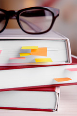 Books with bookmarks and glasses on table on bright background